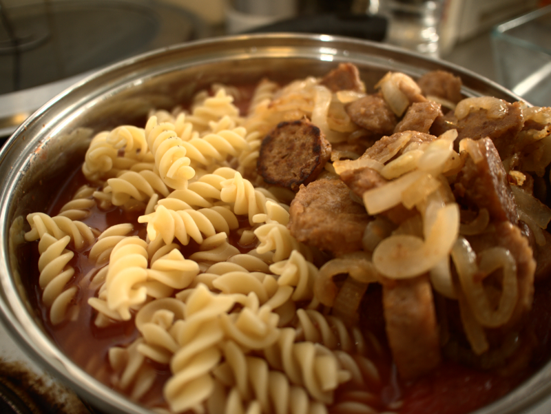 Pre-soaked pasta, sausages, onions, tomato sauce, ready for mixing before baking.