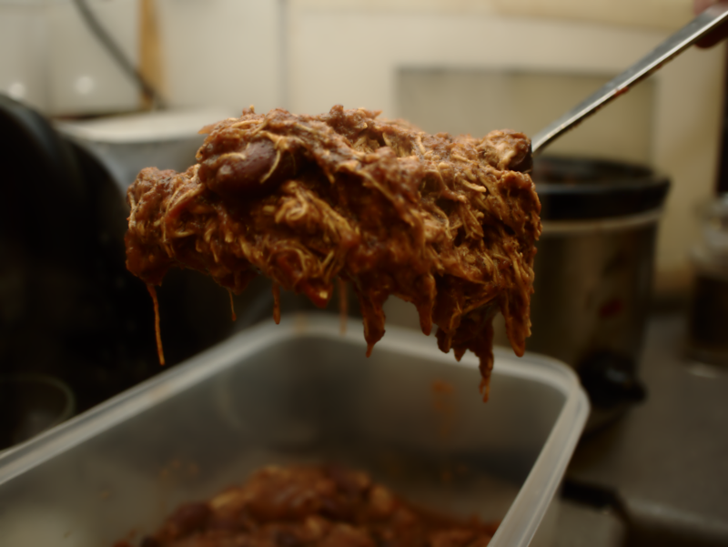 Shredded chicken getting spooned into a lunchbox